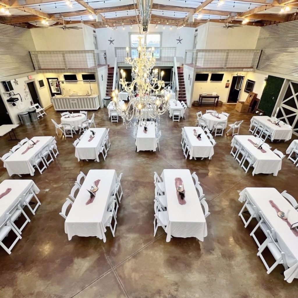 An aerial view of an elegant event space with white-clothed tables, white chairs, and a crystal chandelier.