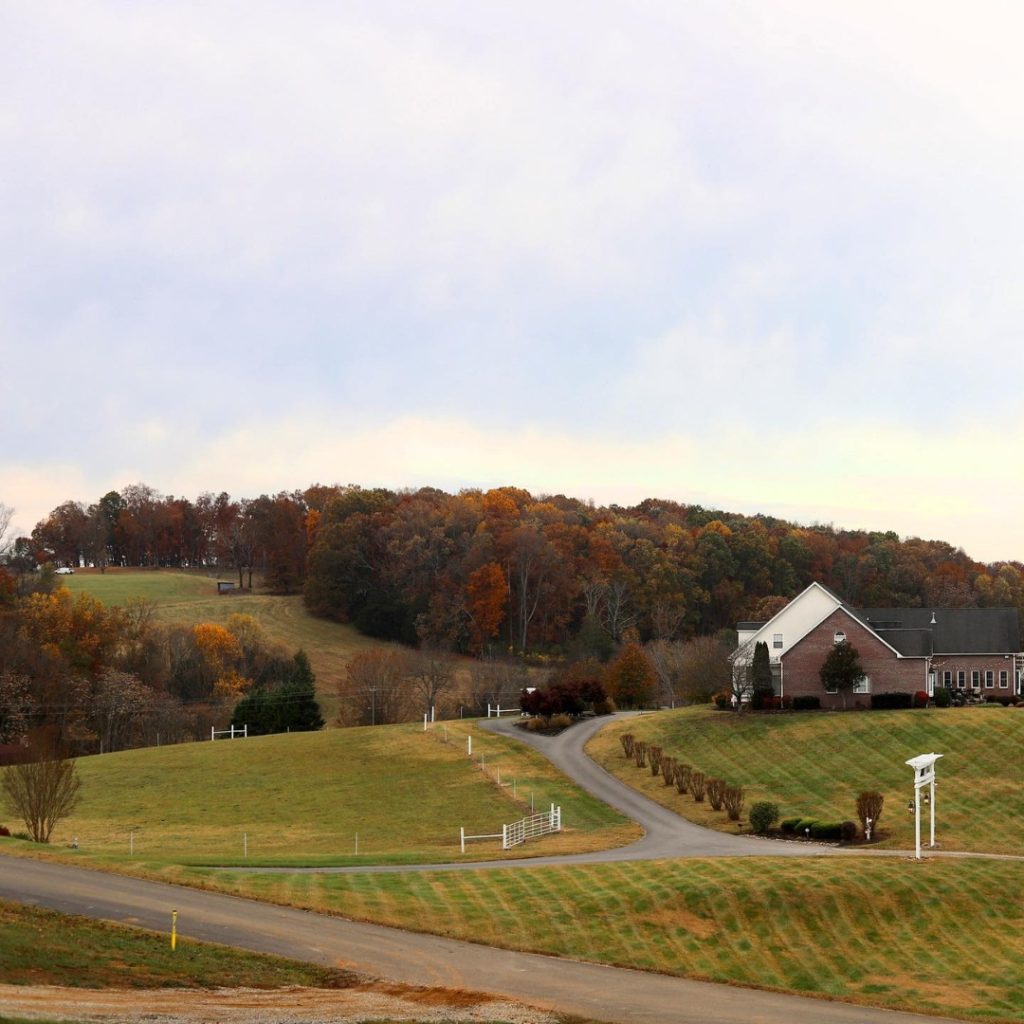 A brick farmhouse with manicured grounds and tree-lined hills under autumn foliage in rural Tennessee.
