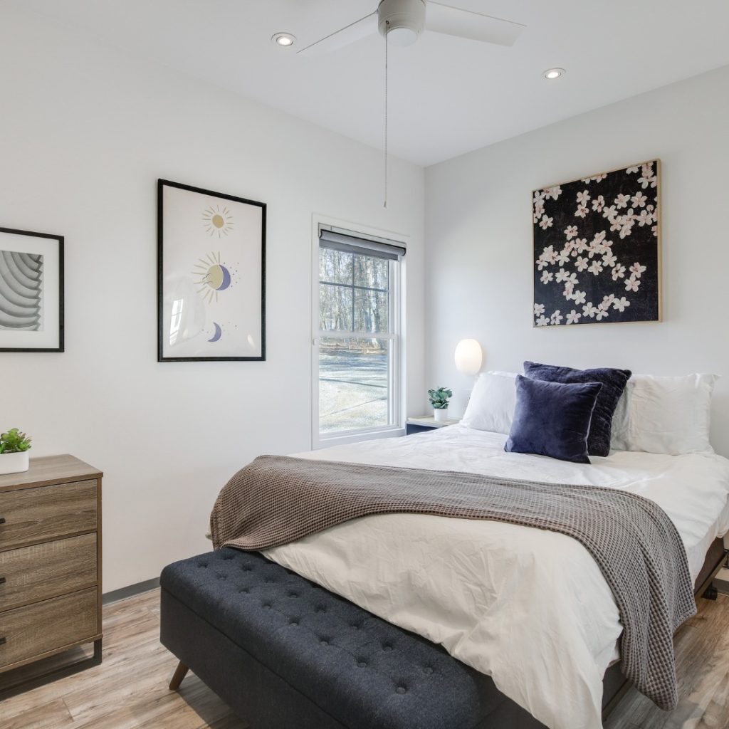 A modern bedroom featuring a bed with white bedding, gray throw blanket, navy pillows, and wooden nightstand.