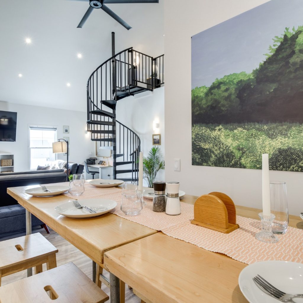 Modern dining room with wooden table, spiral staircase, and nature photography on the wall.