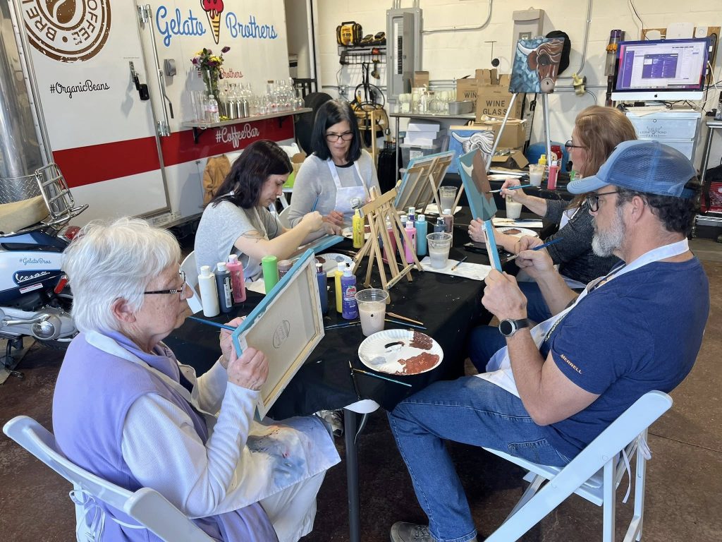 A group of people paint at easels during an art class in a farm studio space.