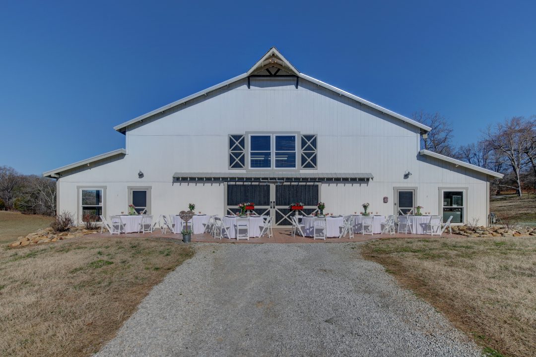 The white barn at Cedar Pond Farms with round tables and white chairs set out front for an all-inclusive retreat.