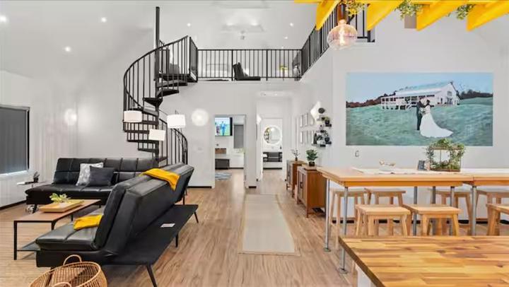 Modern loft interior with spiral staircase, black furniture, wooden dining table, and wedding photo on wall.