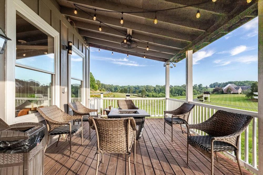 A covered farm porch set with chairs and a table, looking out over green pasture