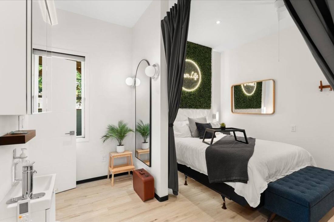 Enjoy this modern European one-bedroom suite in our barndominium at the fluffy cow farm just outside the Smoky Mountains — queen bed, glowing greenery wall and a dressing mirror by the door.