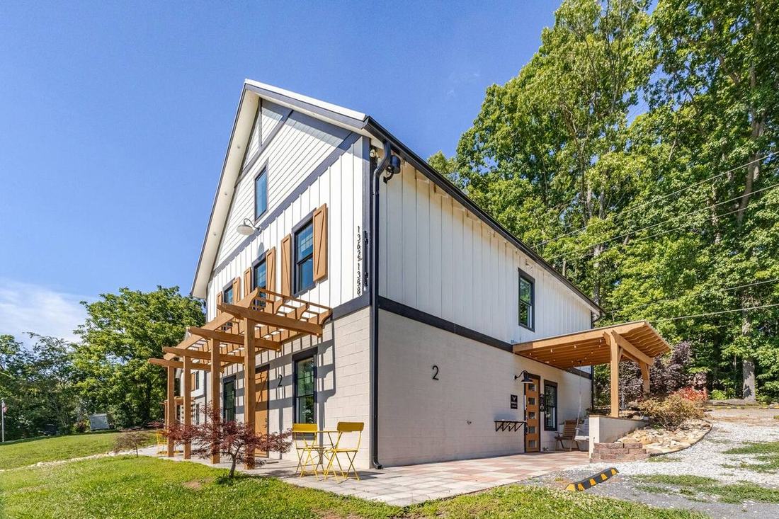 Step up to our white board-and-batten barndominium, where a cedar pergola shades each suite door, at the fluffy cow farm just outside the Smoky Mountains.