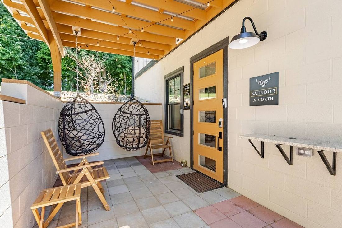 Claim a hanging egg chair on the private porch of Barndo 3 A North — pergola, string lights and a granite drink ledge at our Highland cow farm near the Smoky Mountains.