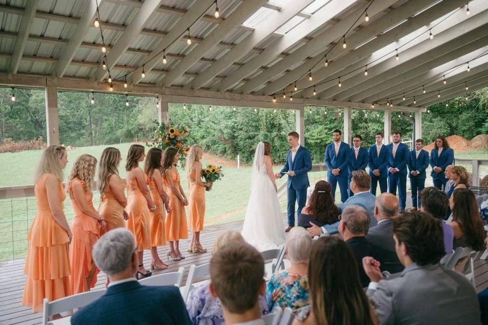 A wedding ceremony under the covered Grand Veranda with bistro lights and farm views