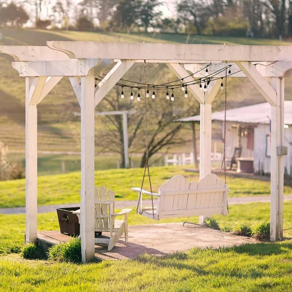 A white flat-wood swing under a Greek-style arbor beside the pond at Cedar Pond Farms